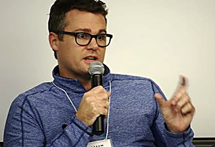 William Skelley speaking with a microphone at an event